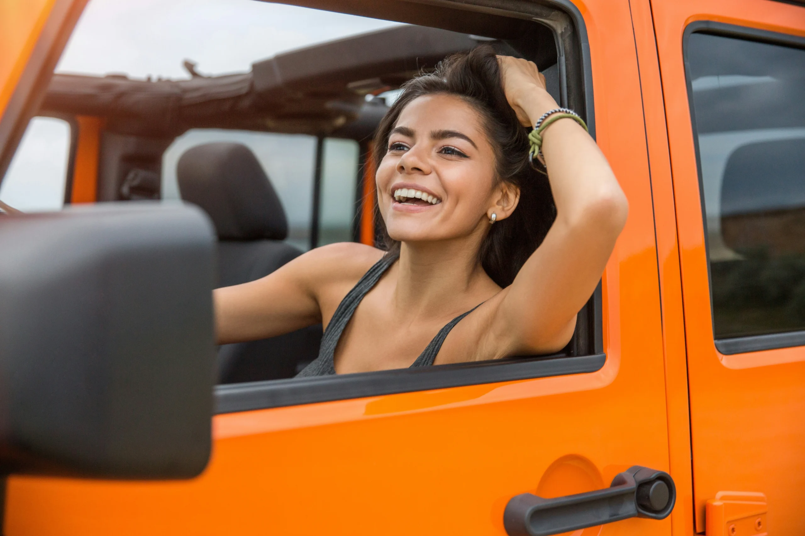 woman looking happy outside the window of her orange car